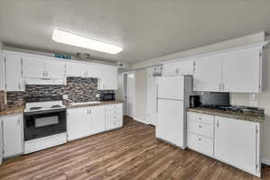 Kitchen featuring white appliances, a textured ceiling, under cabinet range hood, backsplash, and wood finished floors