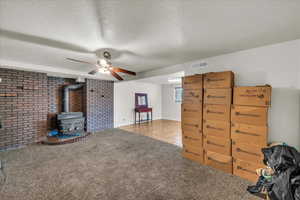 Living area with a wood stove, ceiling fan, carpet, a textured ceiling, and brick wall