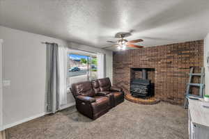 Living room featuring a wood stove, ceiling fan, carpet floors, a textured ceiling, and brick wall