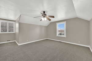 Bonus room featuring lofted ceiling, ceiling fan, carpet flooring, and a textured ceiling