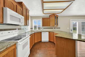 Kitchen featuring white appliances, a peninsula, dark wood finished floors, glass insert cabinets, and a textured ceiling