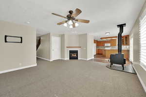 Unfurnished living room featuring a wood stove, light colored carpet, and a ceiling fan