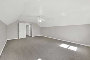 Additional living space featuring dark carpet, lofted ceiling, and a ceiling fan