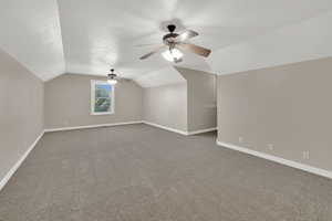 Additional living space featuring dark colored carpet, vaulted ceiling, and ceiling fan