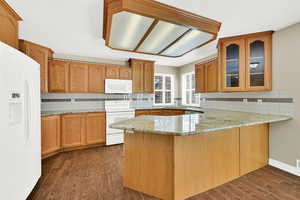 Kitchen featuring white appliances, a peninsula, glass insert cabinets, light stone countertops, and decorative backsplash