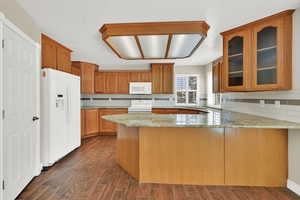 Kitchen featuring white appliances, a peninsula, light stone counters, glass insert cabinets, and tasteful backsplash
