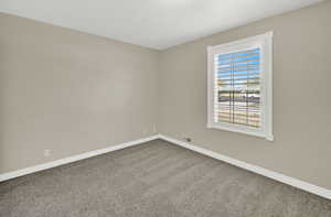 Spare room featuring dark colored carpet and baseboards