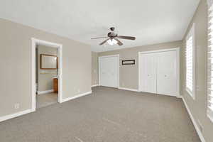 Unfurnished bedroom with multiple closets, carpet, a textured ceiling, connected bathroom, and a ceiling fan