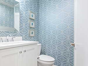 Half bathroom featuring wallpapered walls and vanity