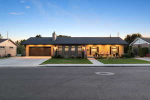 Single story home with concrete driveway, a garage, a chimney, and a front lawn