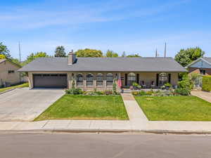 Single story home featuring covered porch, an attached garage, a front yard, a chimney, and driveway