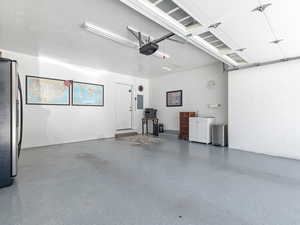 Garage with freestanding refrigerator, electric panel, a garage door opener, and concrete block wall