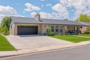 Ranch-style home with a garage, a front yard, concrete driveway, a chimney, and covered porch