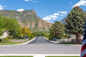 View of asphalt road with curbs, a mountain view, street lights, and sidewalks
