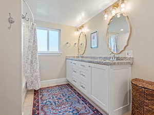 Full bath featuring double vanity, a textured ceiling, and shower / bath combo with shower curtain