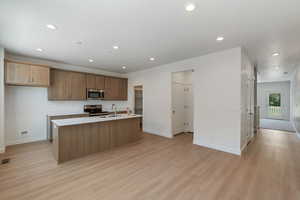 Kitchen with recessed lighting, light wood-type flooring, light countertops, a kitchen island with sink, and appliances with stainless steel finishes