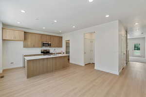 Kitchen featuring light wood-type flooring, recessed lighting, a center island with sink, light countertops, and appliances with stainless steel finishes