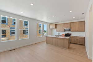 Kitchen featuring light wood-style flooring, appliances with stainless steel finishes, recessed lighting, a kitchen island with sink, and light countertops