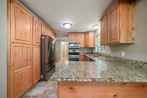 Kitchen with appliances with stainless steel finishes, light stone counters, and a peninsula
