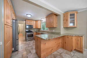 Kitchen featuring appliances with stainless steel finishes, a peninsula, a textured ceiling, light stone finish floors, and light stone counters