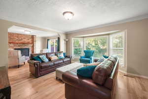 Living area with a textured ceiling, light wood-type flooring, ornamental molding, a fireplace, and arched walkways