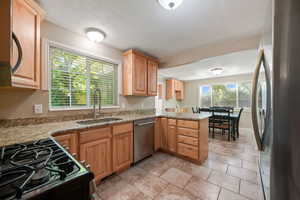 Kitchen featuring stainless steel appliances, light stone countertops, a peninsula, light brown cabinets, and a textured ceiling