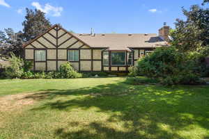 Rear view of house with a lawn, roof with shingles, a chimney, and stucco siding