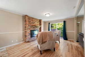 Living area featuring light wood-type flooring, a textured ceiling, a fireplace, and crown molding