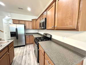 Kitchen featuring stainless steel appliances, brown cabinets, light wood-style floors, dark countertops, and recessed lighting