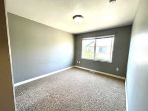 Carpeted spare room with a smoke detector and a textured ceiling