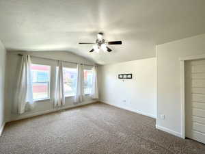 Carpeted empty room featuring a ceiling fan and vaulted ceiling