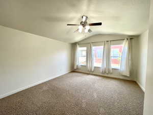 Spare room featuring ceiling fan, vaulted ceiling, and carpet