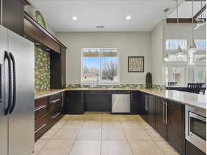 Kitchen with appliances with stainless steel finishes, light countertops, light tile patterned flooring, decorative backsplash, and dark brown cabinetry