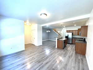 Kitchen featuring stainless steel appliances, open floor plan, a chandelier, a kitchen island with sink, and light wood-style flooring