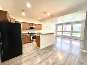 Kitchen featuring stainless steel appliances, light wood finished floors, open floor plan, brown cabinetry, and recessed lighting