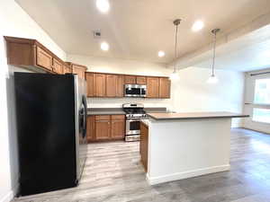 Kitchen featuring stainless steel appliances, brown cabinets, light wood-style floors, hanging light fixtures, and recessed lighting