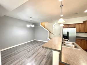 Kitchen featuring stainless steel refrigerator with ice dispenser, brown cabinetry, wood finished floors, hanging light fixtures, and a chandelier