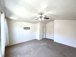 Empty room with a ceiling fan, vaulted ceiling, and dark carpet