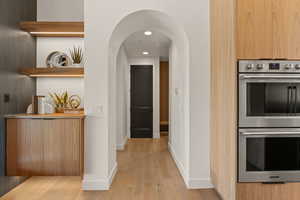 Kitchen with stainless steel double oven, recessed lighting, arched walkways, light wood-style floors, and open shelves