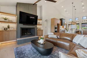 Living room featuring high vaulted ceiling, ceiling fan, light wood-type flooring, a fireplace, and recessed lighting
