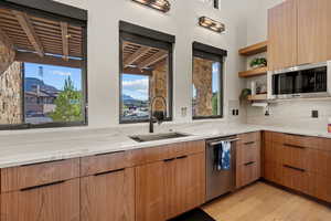 Kitchen with modern cabinets, open shelves, light stone counters, appliances with stainless steel finishes, and light wood-style flooring