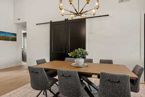 Dining room with a barn door, light wood-style floors, a chandelier, and a towering ceiling