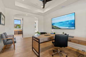 Office space featuring arched walkways, a tray ceiling, light wood-style flooring, recessed lighting, and ceiling fan