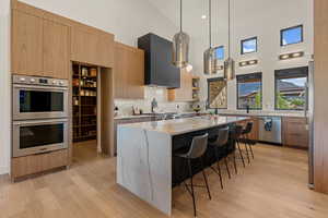 Kitchen featuring a high ceiling, appliances with stainless steel finishes, light stone counters, modern cabinets, and pendant lighting