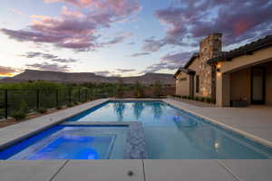 Pool at dusk with a mountain view, a fenced backyard, a patio area, and a pool with connected hot tub