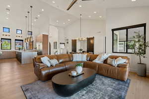 Living area with high vaulted ceiling, light wood finished floors, recessed lighting, a chandelier, and healthy amount of natural light