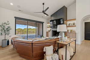 Living room featuring light wood-style flooring, a ceiling fan, a large fireplace, recessed lighting, and arched walkways