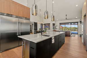 Kitchen with modern cabinets, built in refrigerator, decorative light fixtures, dark cabinetry, and light wood finished floors