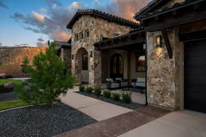 Exterior entry at dusk with stone siding, a porch, a tile roof, and stucco siding