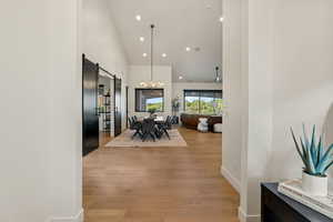 Dining space featuring a barn door, high vaulted ceiling, recessed lighting, light wood finished floors, and a chandelier